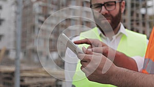 Close up of architect hands using tablet near construction site. The builder and architect man are discussing the