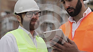 Close up of architect hands using tablet near construction site. The builder and architect man are discussing the