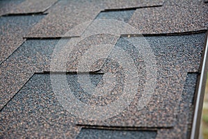 A close-up on architectural asphalt shingles installed on a roof.  Brown dimensional asphalt shingles roofing background