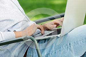 Close up arms of blogger man with laptop working outdoors in garden, sitting on chair.