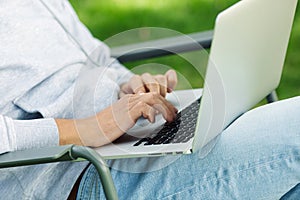 Close up arms of blogger man with laptop working outdoors in garden, sitting on chair.