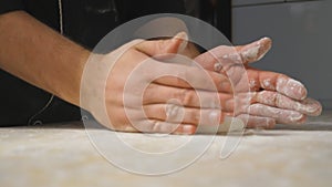 Close up arms of cook forming pastry on a wooden surface at cuisine. Male hands of chef shaping floured dough for pizza