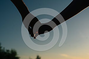 Close-up arms of loving young couple hand-holding and walking towards sunset on background of cloudless sky in evening.