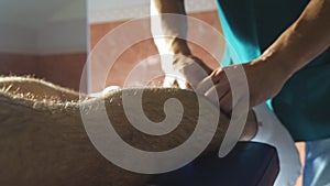 Close up arms of professional masseur doing slowly rubdown leg of athlete lying on massage table in salon. Male hands of