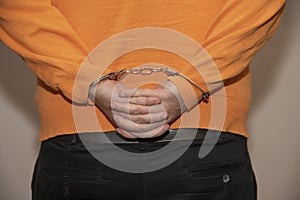 Close-up. Arrested man handcuffed hands at the back isolated on gray background