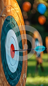 Close-up of an arrow nailing the bullseye on a rustic wooden archery target, with blurred balloons creating a whimsical