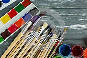 Close up of artist paint brushes, palette and watercolors on grunge gray wooden background.