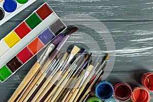 Close up of artist paint brushes, palette and watercolors on grunge gray wooden background.