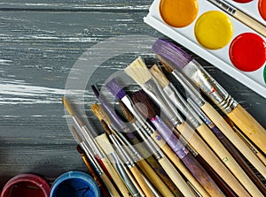 Close up of artist paint brushes, palette and watercolors on grunge gray wooden background.