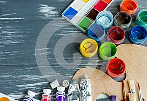 Close up of artist paint brushes, palette and watercolors on grunge gray wooden background.