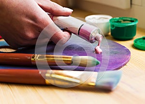 Close-up of the artist's hand squeezed from a tube paint on an easel. Brushes, paints, an easel on the table