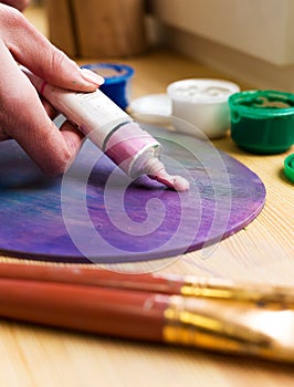 Close-up of the artist's hand squeezed from a tube paint on an easel. Brushes, paints, an easel on the table