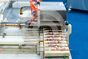 Close up asia barbecued or pork stick on support rail of automatic or stab pork machine for industrial manufacturing