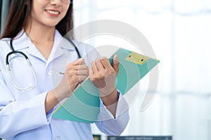 Close up of Asian beautiful female doctor in white coat with stethoscope holding chart sheet , waist up. Medical student. Medical