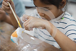 Close up asian child girl is concentrating to paint on small ceramic elephant with oil color.