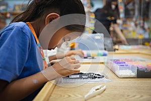 Close up on asian child girl hand making fusible beads thermo mosaic in pegboard that is a toy to develops the imagination of