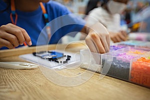 Close up on asian child girl hand making fusible beads thermo mosaic in pegboard that is a toy to develops the imagination of