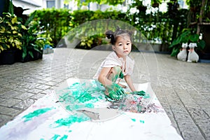 Close up Asian child girl sit down on rip canvas on tile floor on blurred garden.