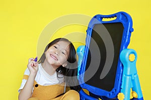 Close up asian little child girl with writing and drawing on empty blackboard over yellow background. Student and development