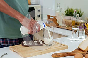 Close-up Asian man's hand standing in kitchen in morning, man opened cap bottle plain cow's milk come out pour it