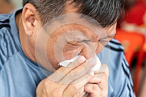 Close-up of Asian man sneezing onto tissue paper, covering mouth and nose. Personal hygiene important