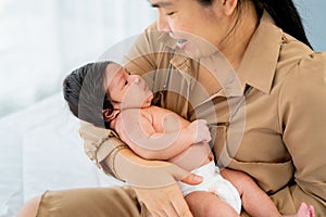 Close up Asian mother hold newborn baby and sit on bed in bedroom with day light and take care also look with love and happiness