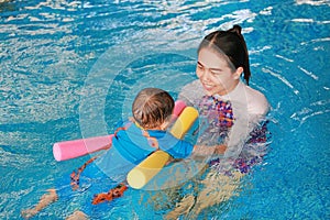 Close-up Asian mother teaching baby boy in swimming pool with noodle foam