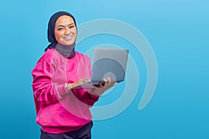 Close up of Asian Muslim girl, holding laptop in hand isolated on blue background photo
