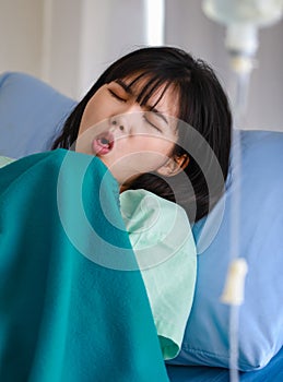 Close-up of an asian sick female patient covered with a blanket lying on hospital bed having intravenous drip saline solution,