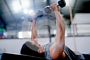 Close up Asian sport man lift dumbells up to over head during lie on long chair in fitness gym