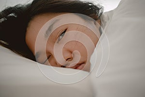 Close up of asian Thai woman closing eyes, sleeping on white bed in the morning in room apartment.
