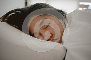 Close up of asian Thai woman closing eyes, sleeping on white bed in the morning in room apartment.