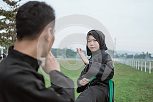 Close up of an Asian woman with a hijab wearing a pencak silat uniform, ready to kick her opponent