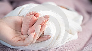 Close up asian woman mother hand holding small baby infant feet while sleeping on soft bed covered with white cloth.
