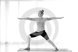 Close up Asian woman practicing yoga, standing in Warrior two exercise, Virabhadrasana II pose on mat,monochrome