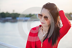 Close up Asian woman in a red jacket posting next to a white fence, She touches her hair with her left hand on the bridge with