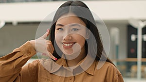 Close up Asian woman smiling japanese chinese korean girl businesswoman pointing finger to camera doing phone gesture