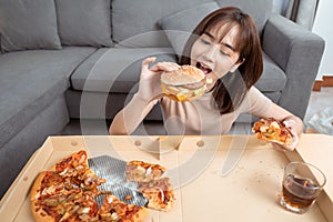 Close up asian woman takeaway eating junk food hamburger and pizza close-up shot in living room