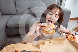 Close up asian woman takeaway eating junk food hamburger and pizza close-up shot in living room