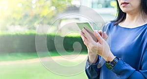 Close up Asian woman using mobile phone outside home in green ga