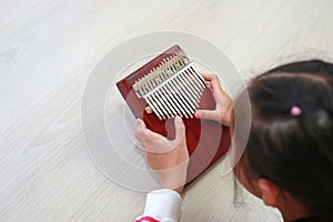 Close-up Asian young hands playing Kalimba Mbira or thumb piano lying on wood floor at home. Rear view
