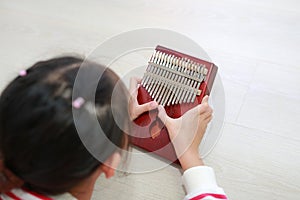 Close-up Asian young hands playing Kalimba Mbira or thumb piano lying on wood floor at home. Rear view