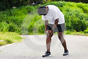 Close up Asian young sport runner black man wear watch stand use hands joint hold knee pain during the run while running at the ou