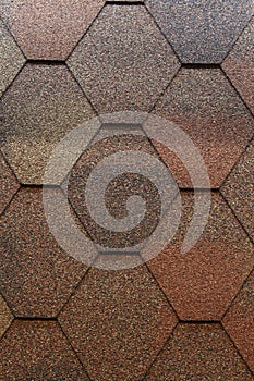 A close-up of asphalt roofing shingles of a diamond shape, and a camouflage, brown color. Diamond-shaped asphalt roofing shingles