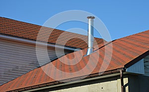 A close-up of an asphalt shingled roof with a stainless steel, metal chimney, coaxial chimney and rain gutters on the roof