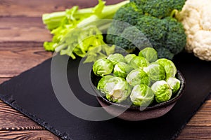 Close up of assorted healthy fresh vegetables on a black slate on a wooden table: cabbage, broccoli, cauliflower and