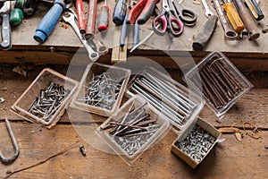 A close up of an assortment of nails, screws and tools on a wooden work bench, natural light