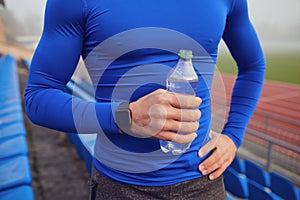 Close up of athlete`s hand with a smartwatch and a bottle of water.