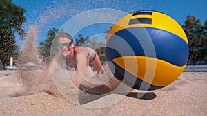 CLOSE UP: Athletic girl playing volleyball dives into the sand to reach the ball