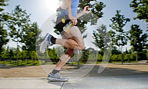 Close up athletic legs of young man running in city park with trees on summer training session practicing sport healthy lifestyle